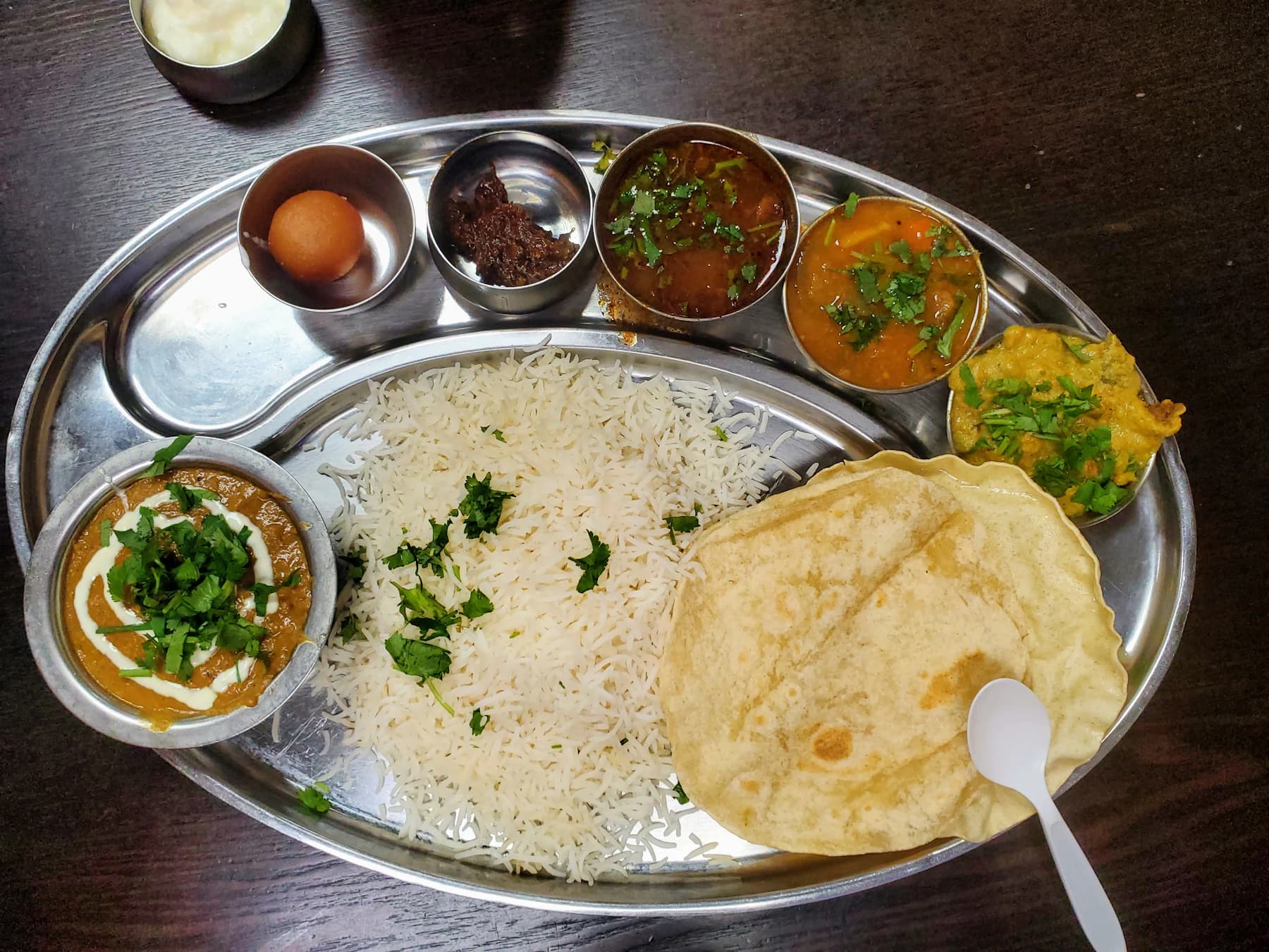 A steel thali with white rice, roti, dal and vegetable curries
